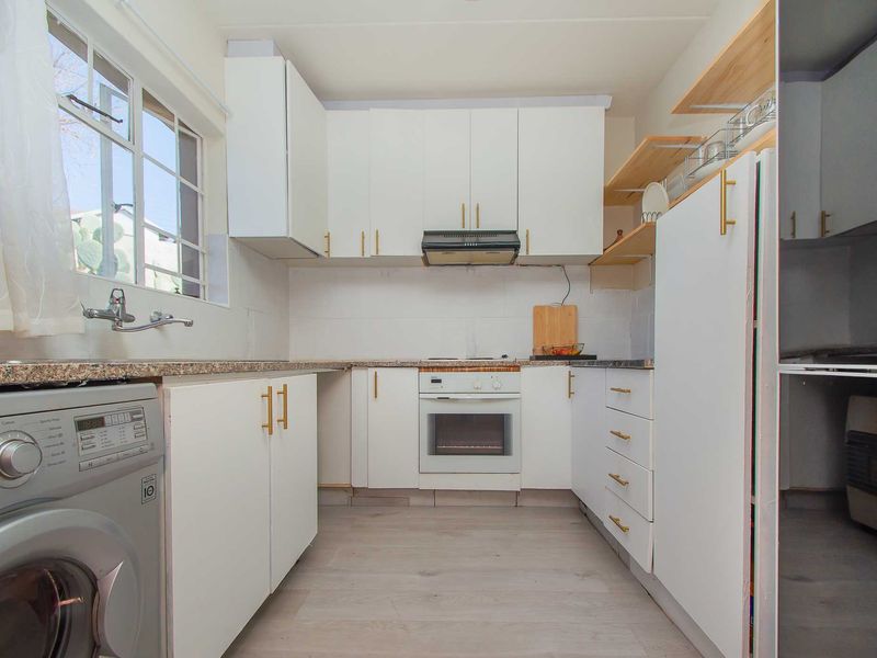 A functional kitchen featuring white cabinetry, granite countertops, built-in oven, extractor fan, and integrated laundry plumbing, offering a clean and practical workspace.