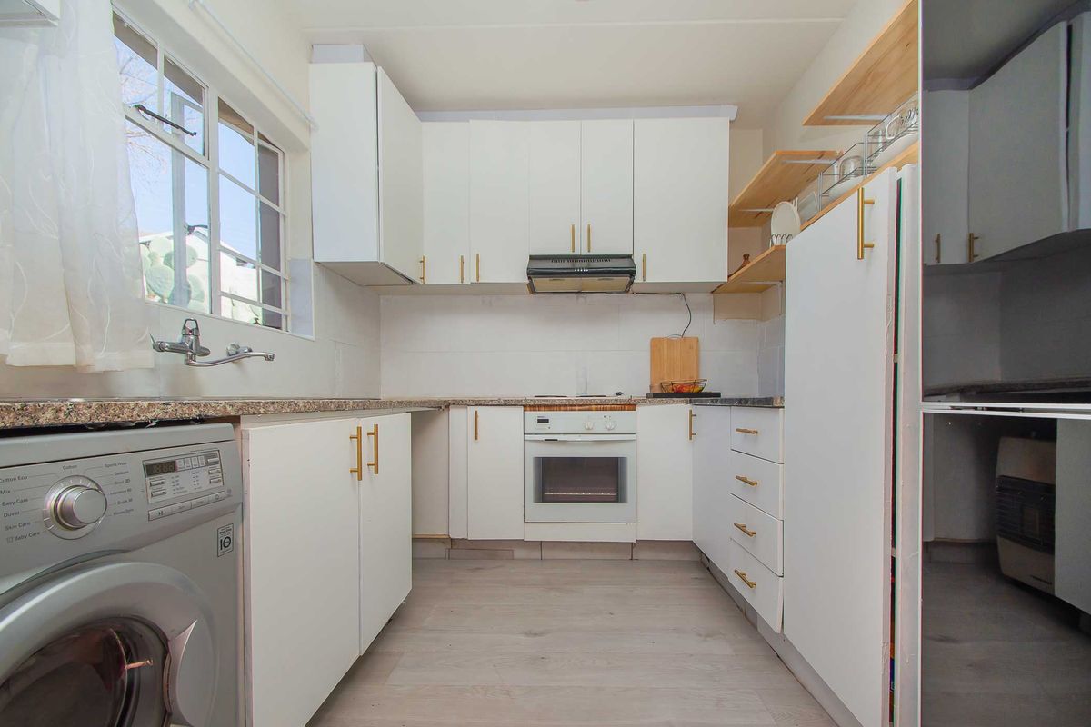 A functional kitchen featuring white cabinetry, granite countertops, built-in oven, extractor fan, and integrated laundry plumbing, offering a clean and practical workspace.