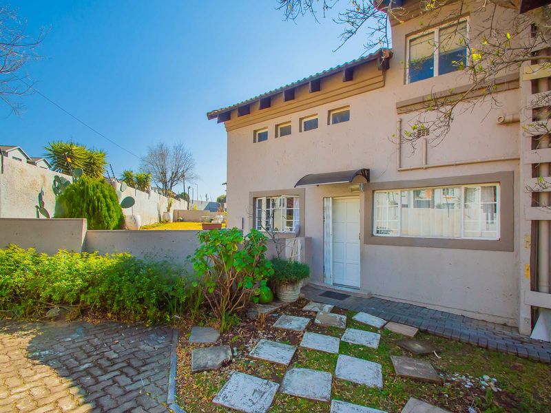 Front exterior view of a two-story apartment unit featuring a paved driveway, stone walkway, and secure boundary wall with electric fencing.