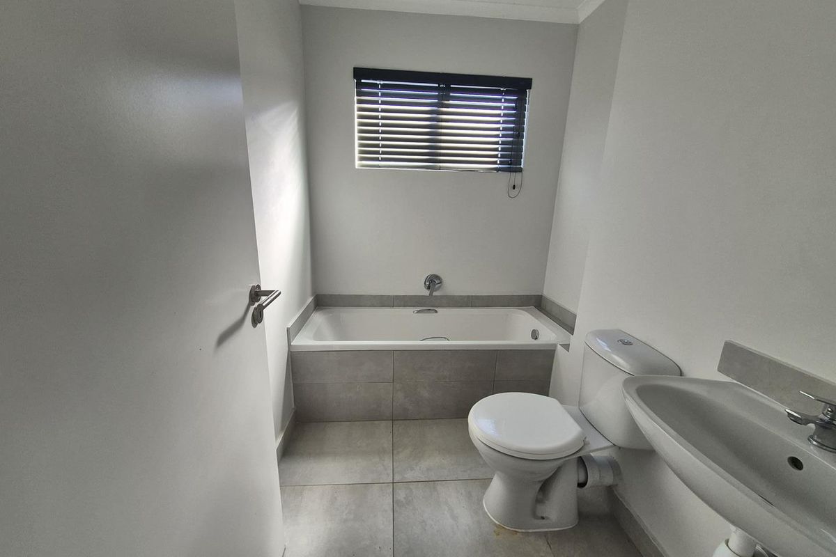 A clean, functional bathroom featuring a built-in bathtub, ceramic floor tiling, a wall-mounted basin, and a toilet with neutral finishes.
