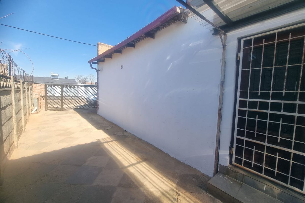 A side exterior view of the property featuring a paved walkway, security gate, and perimeter walling.