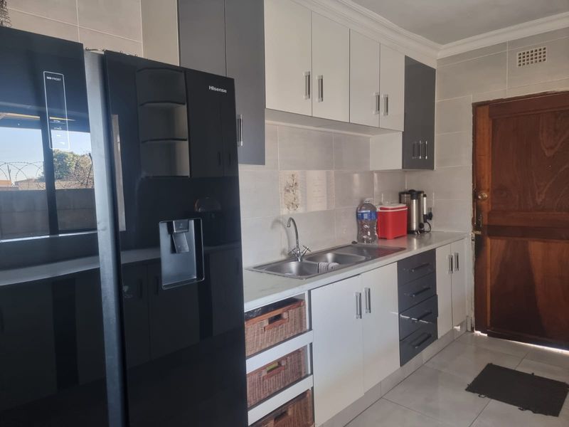 A functional kitchen featuring modern two-tone cabinetry, a double sink, tiled backsplash, and tiled flooring with direct access to an exterior door.