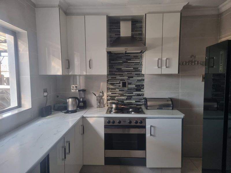 Modern kitchen featuring white cabinetry, marble-look countertops, a stainless steel extractor fan, built-in oven, gas hob, and a stylish mosaic tile backsplash.