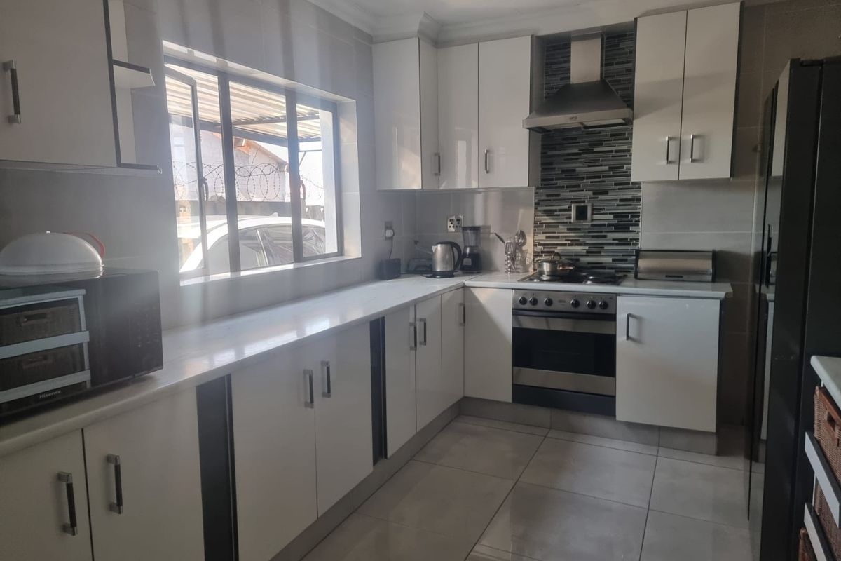 Modern kitchen featuring white built-in cabinetry, stone countertops, stainless steel oven with extractor fan, and tiled flooring.