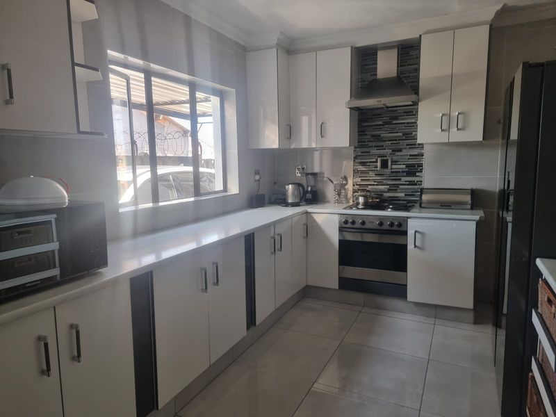 Modern kitchen featuring white built-in cabinetry, stone countertops, stainless steel oven with extractor fan, and tiled flooring.