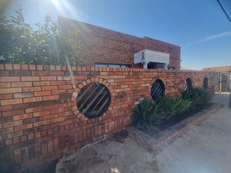 Front exterior view featuring a face brick boundary wall with circular decorative inserts and a concrete driveway leading to the property entrance.