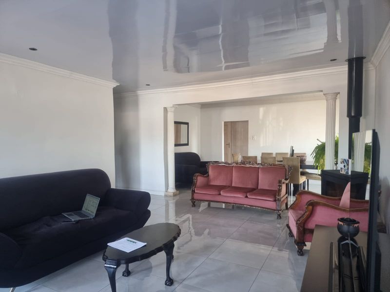 Spacious open-plan living and dining area featuring glossy ceilings, tiled floors, decorative columns, and a modern freestanding fireplace.
