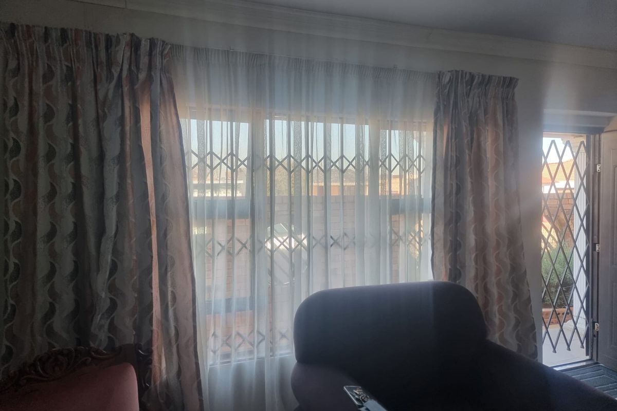 A living room area featuring a large window with security gate and an adjacent door leading to the exterior.