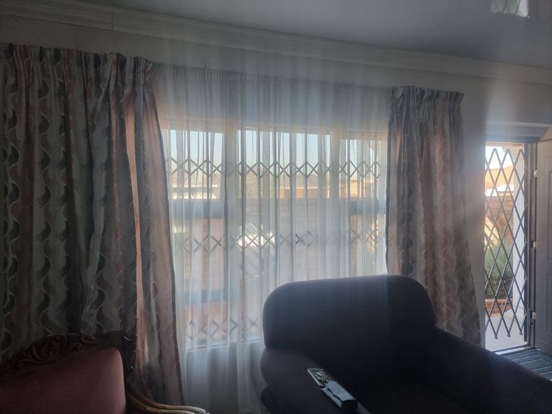 A living room area featuring a large window with security gate and an adjacent door leading to the exterior.