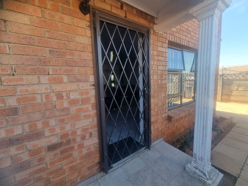 Front entrance area featuring a brick facade, security gate, tiled porch, and a decorative column.