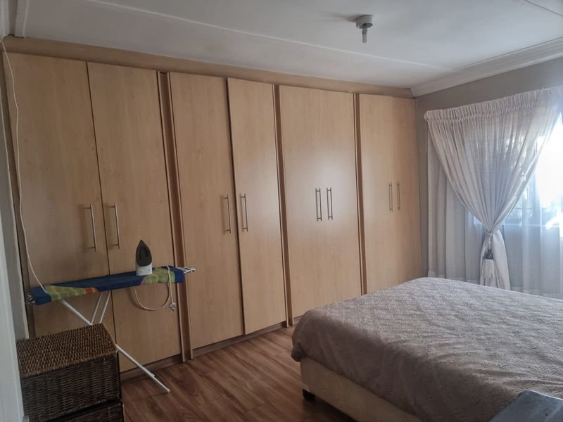 A bedroom featuring extensive light wood-finish built-in wardrobes, laminate flooring, and natural light through a window with curtains.