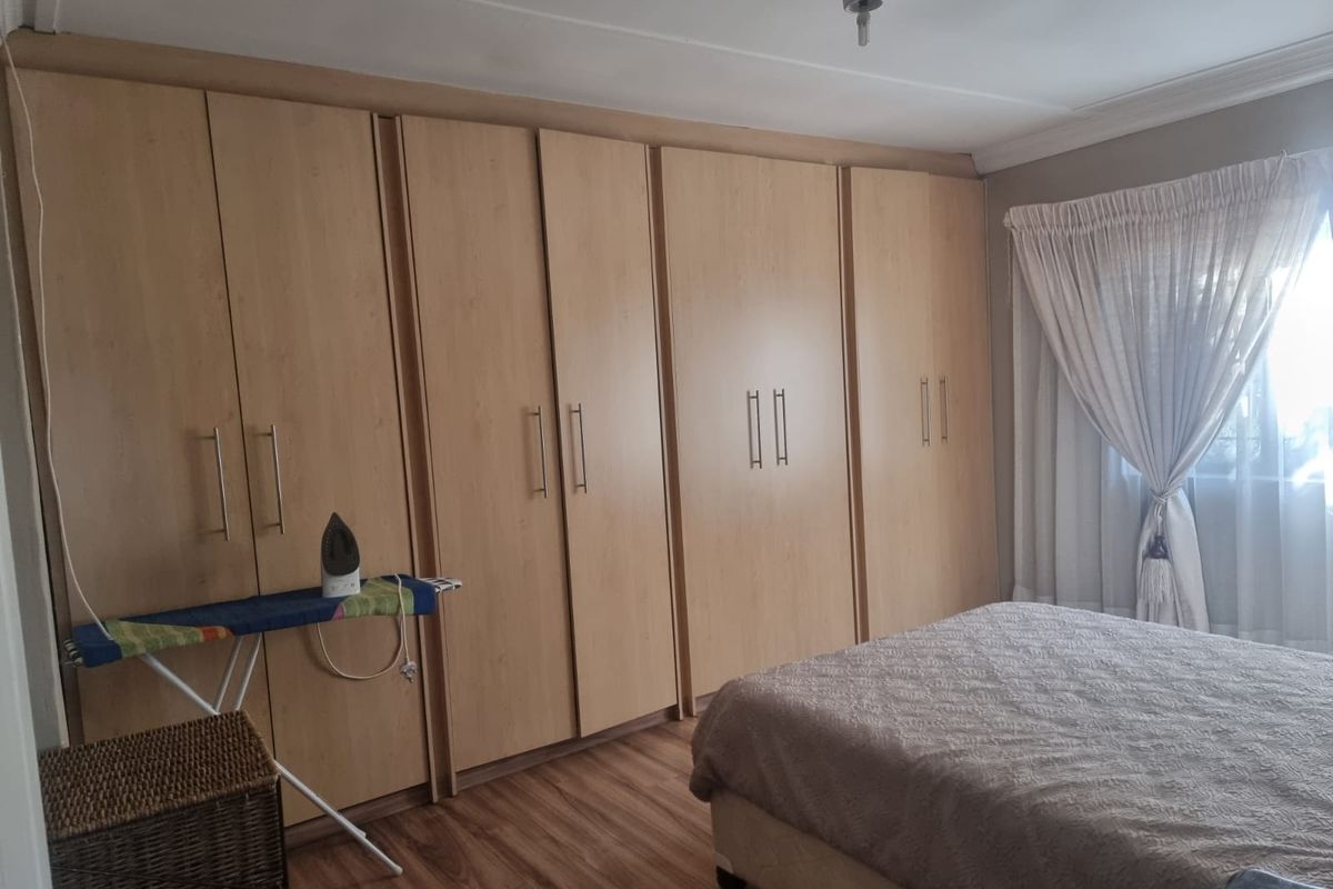 A bedroom featuring extensive light wood-finish built-in wardrobes, laminate flooring, and natural light through a window with curtains.