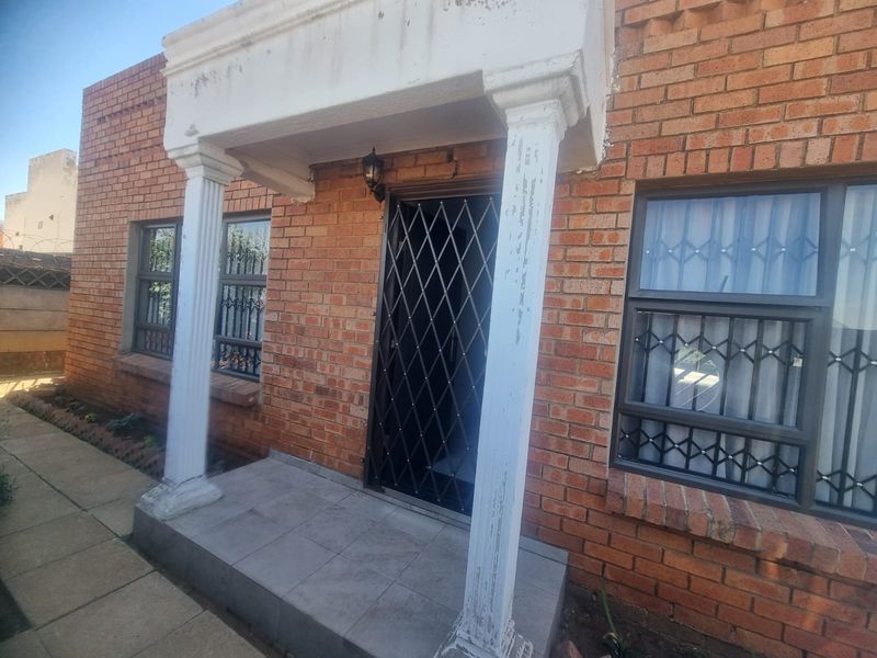 Front entrance of a brick house featuring a tiled porch, decorative columns, and security gates on the door and windows.