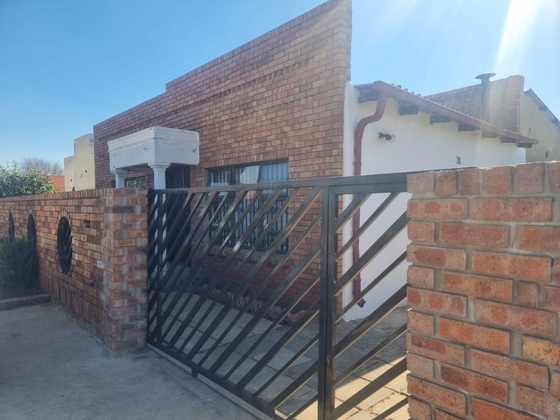 Front exterior view of a face brick house featuring a secure metal sliding gate, brick boundary wall, and a concrete driveway.