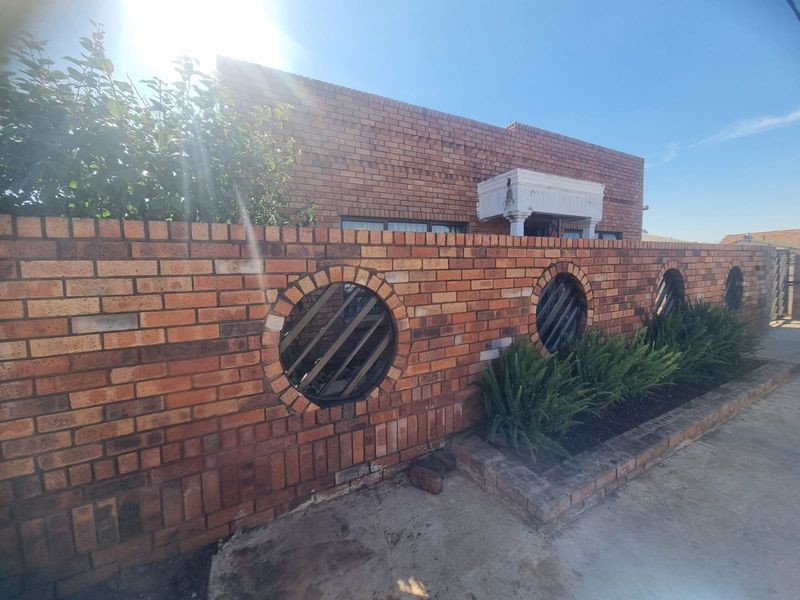 Front view of the property featuring a distinctive face brick boundary wall with circular decorative elements and a concrete driveway.