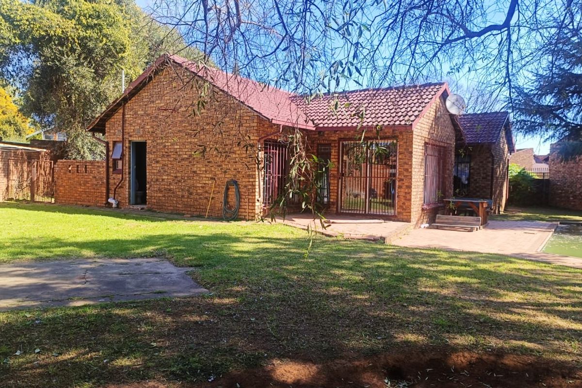 Rear view of a face-brick house featuring a tiled roof, paved patio area, and a swimming pool set within a private garden.