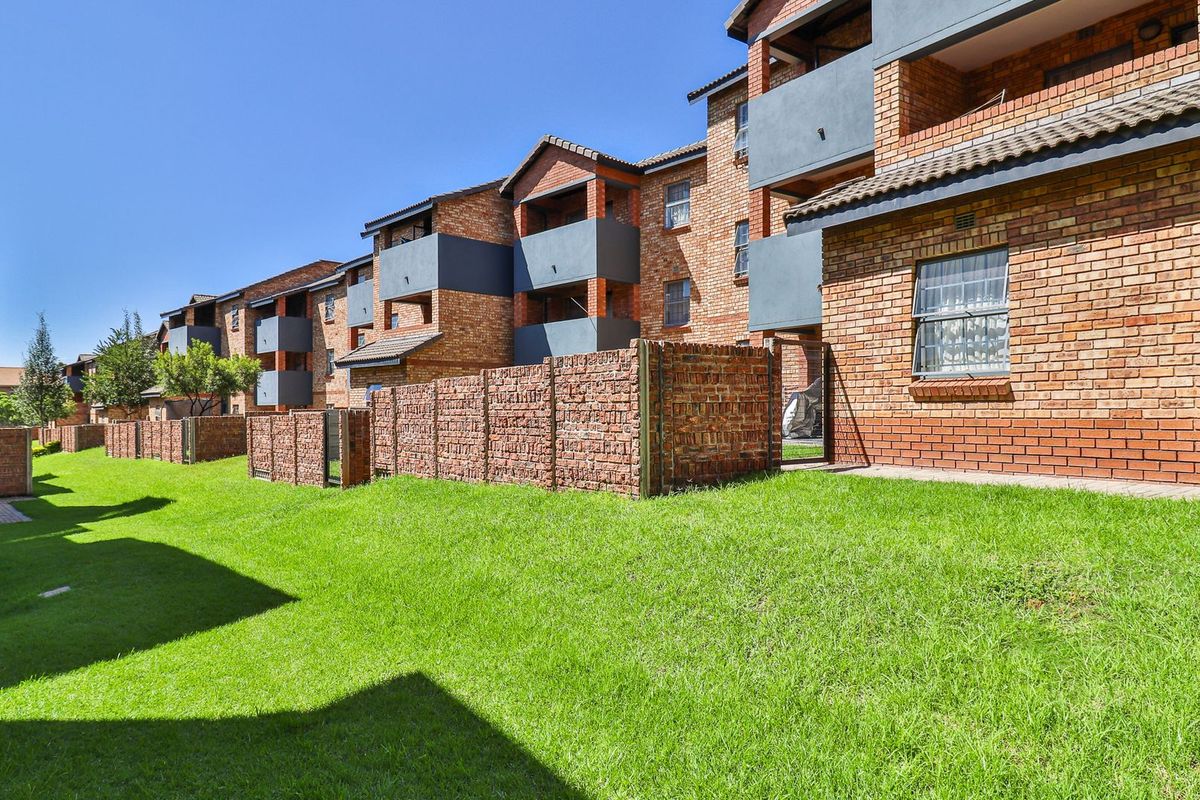 A view of the rear elevation of a face brick apartment complex featuring private balconies and a well-maintained communal garden area.