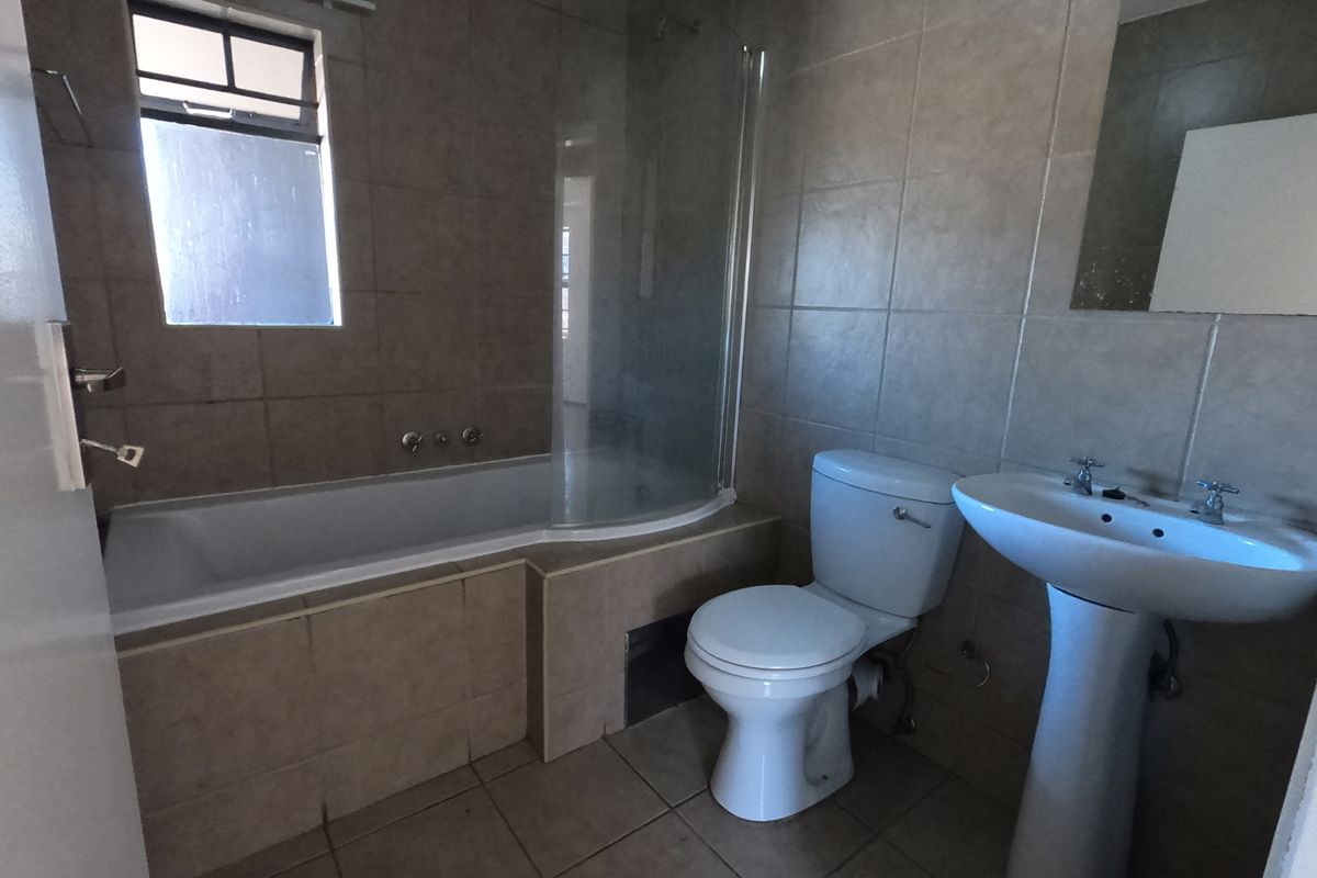 A functional bathroom featuring a bathtub with a glass screen, pedestal basin, and toilet, finished with neutral wall and floor tiles.