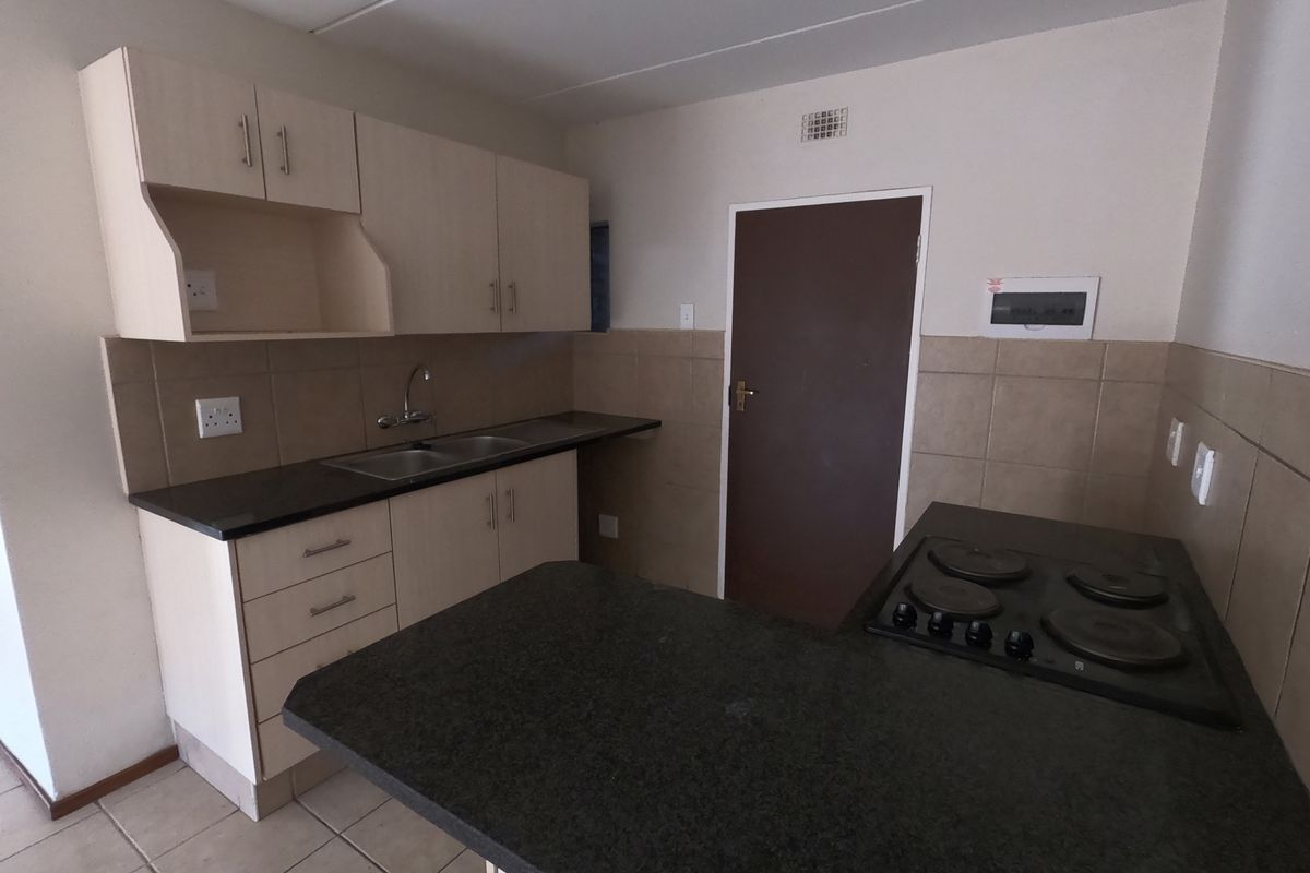 Functional kitchen featuring laminate cabinetry, granite countertops, a double basin sink, and a built-in electric hob with tiled backsplash.
