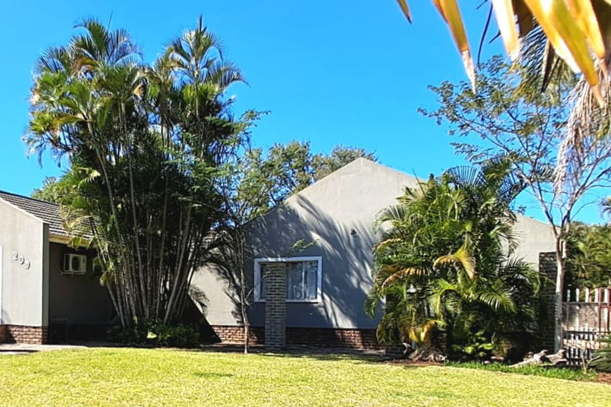Rear view of the property featuring a plastered facade, tiled roof, and a well-maintained garden area with mature palm trees.