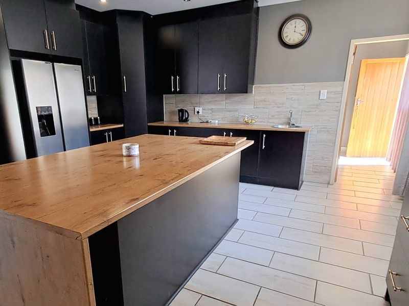 Modern kitchen featuring dark cabinetry, a wooden-topped central island, tiled backsplash, and built-in oven, offering a functional and contemporary cooking space.