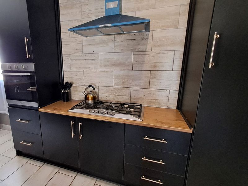 Modern kitchen featuring matte black cabinetry, a wooden countertop, gas hob, built-in oven, and a stylish tiled backsplash with an extractor fan.