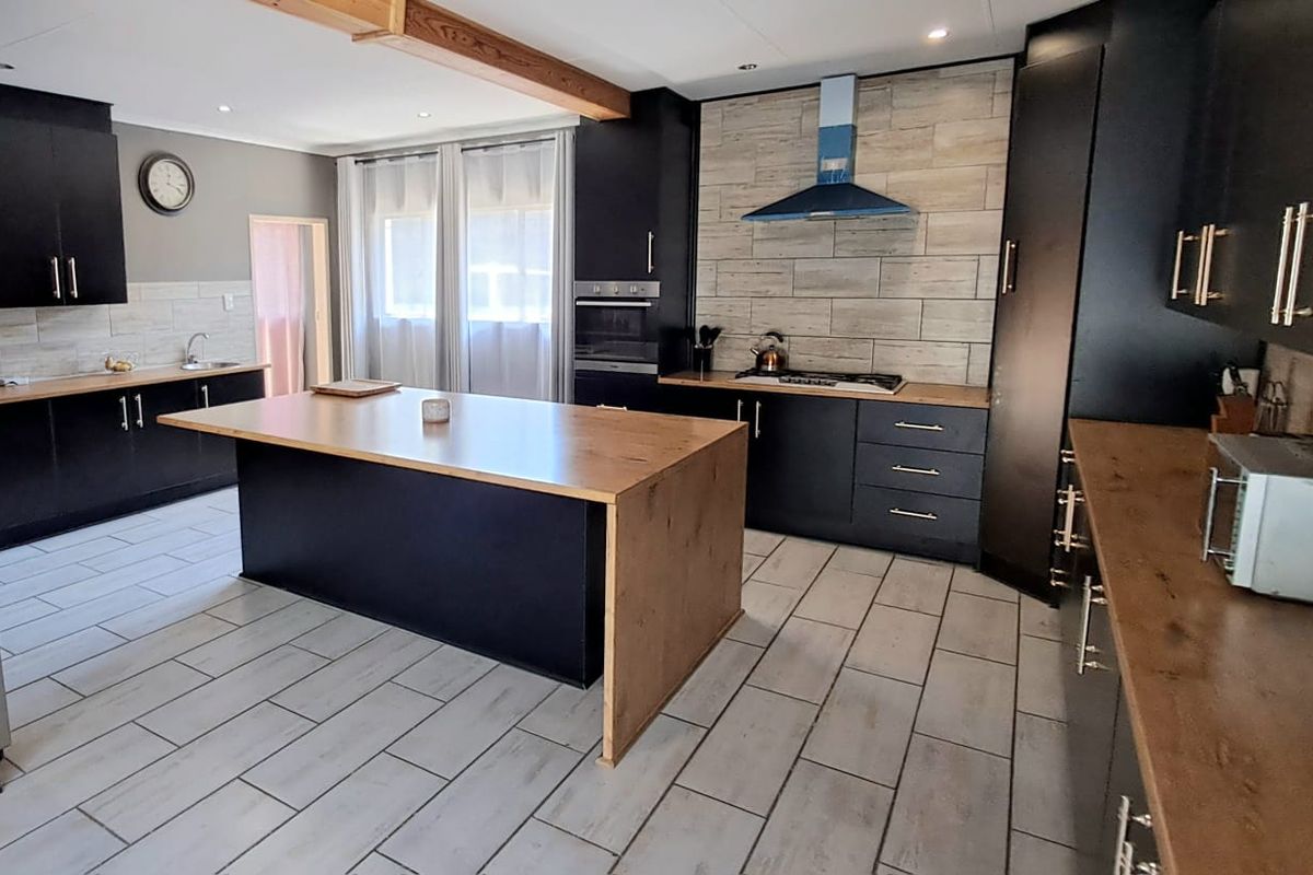 Modern kitchen featuring a large central island, dark cabinetry, wood-look countertops, tiled flooring, and integrated appliances with a stylish tiled backsplash.