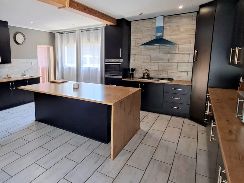 Modern kitchen featuring a large central island, dark cabinetry, wood-look countertops, tiled flooring, and integrated appliances with a stylish tiled backsplash.