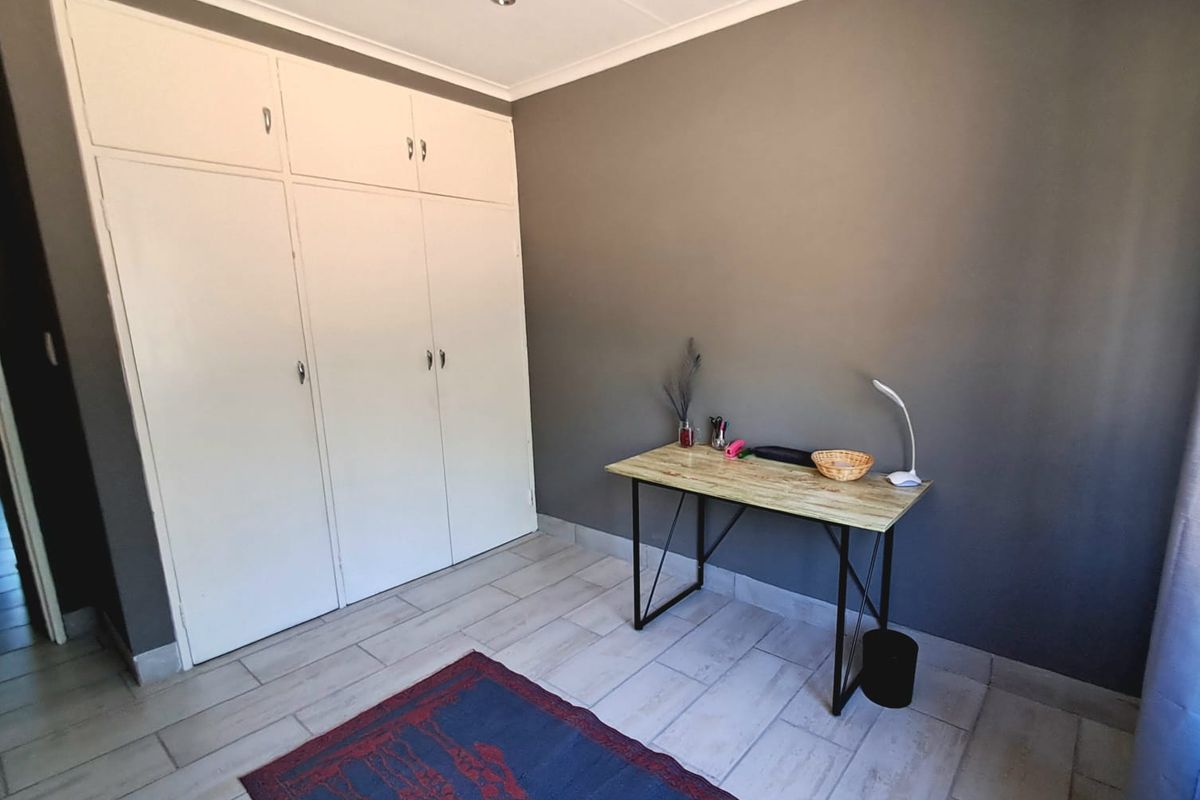 A bedroom featuring built-in cupboards, tiled flooring, and neutral grey wall finishes, providing a functional and clean living space.