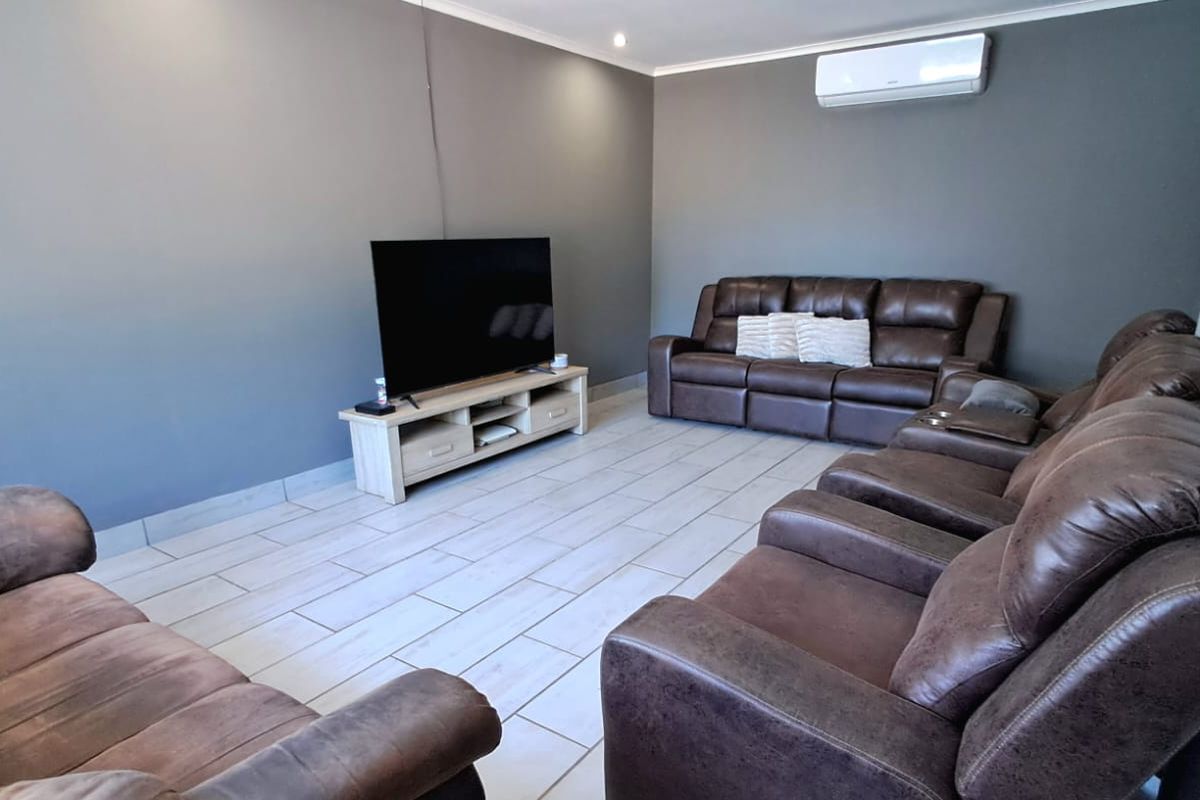 A well-maintained living room featuring neutral grey walls, light-toned tiled flooring, and a wall-mounted split-system air conditioning unit.
