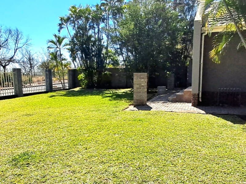A well-maintained private garden featuring a lush lawn, perimeter fencing, and a small paved patio area adjacent to the house.