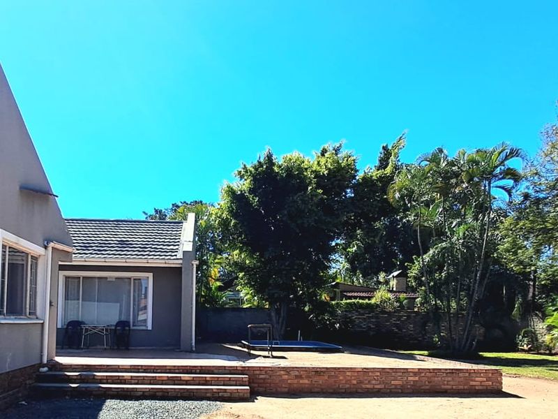 Rear view of the property featuring a brick patio, swimming pool, and established garden with a boundary wall.