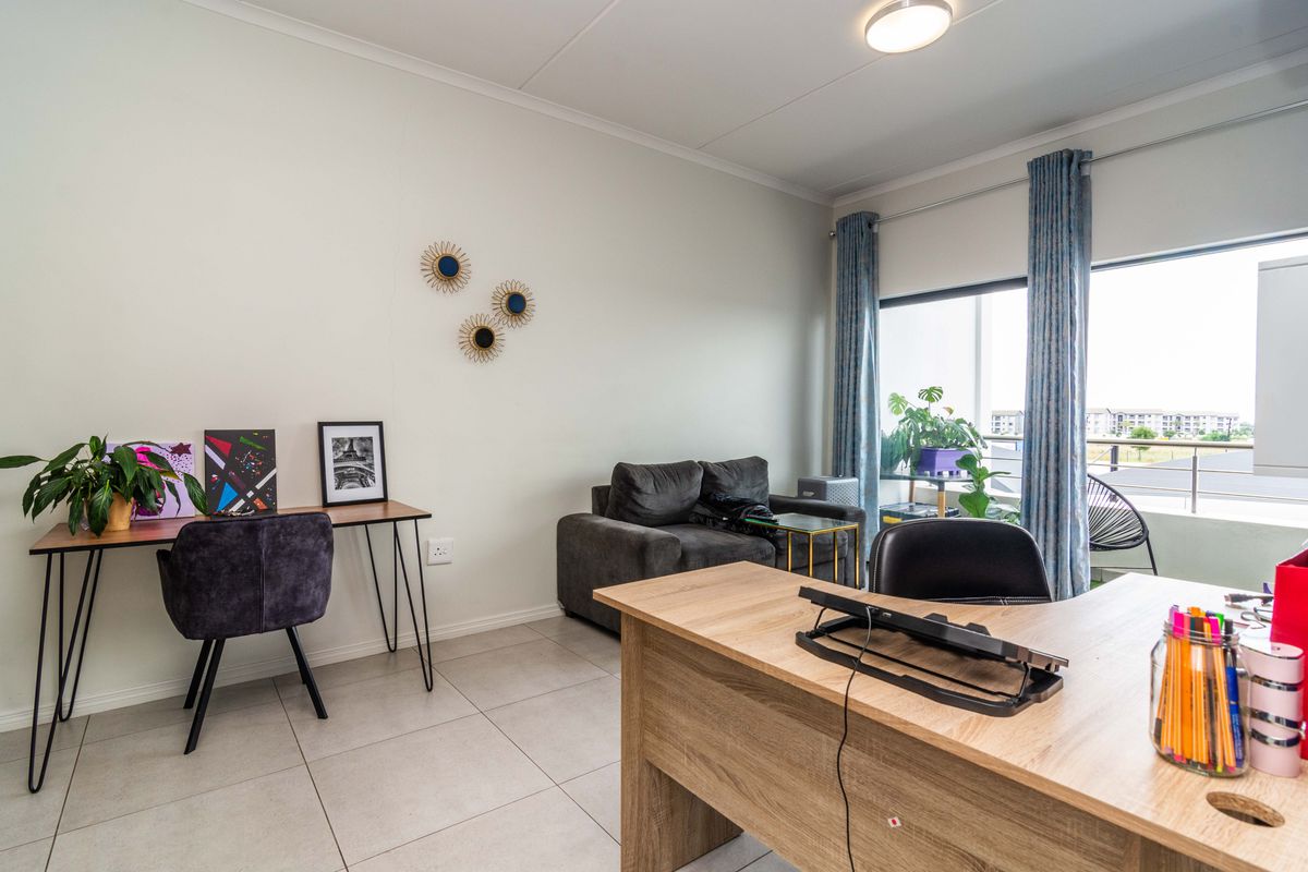 A bright living area featuring neutral tiled flooring, a large sliding glass door providing natural light, and access to an outdoor balcony.