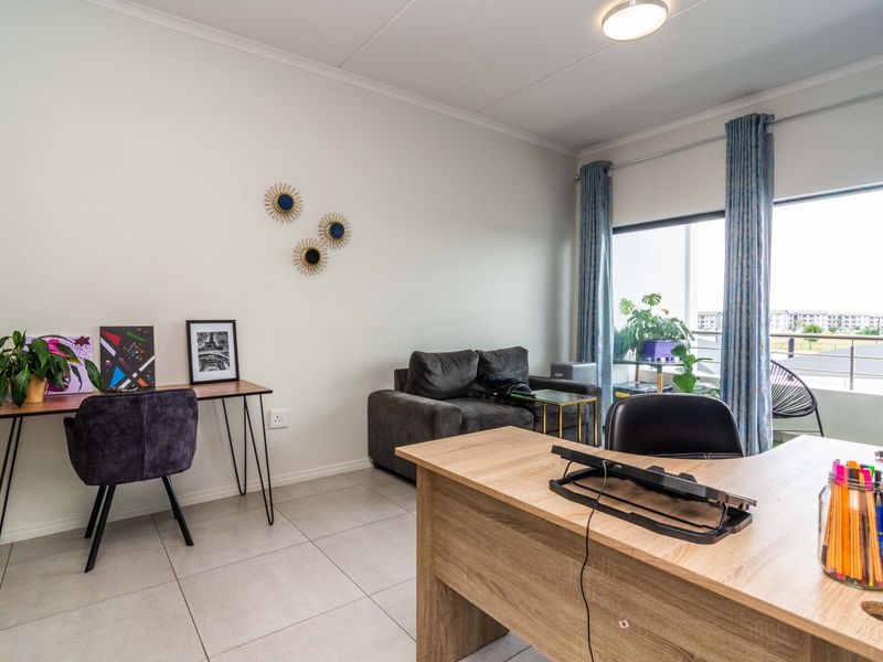 A bright living area featuring neutral tiled flooring, a large sliding glass door providing natural light, and access to an outdoor balcony.