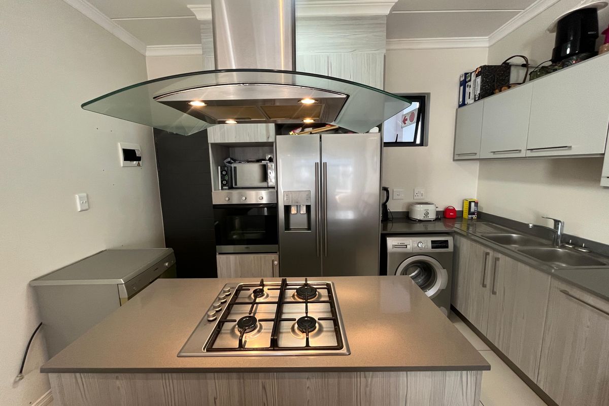 Modern kitchen featuring a central island with a gas hob, stainless steel extractor fan, built-in oven, and integrated laundry appliances.