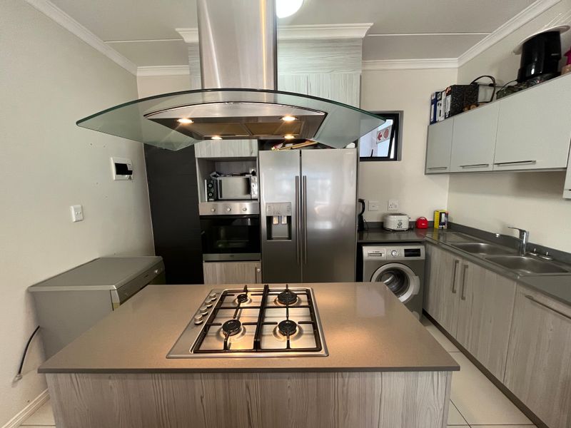 Modern kitchen featuring a central island with a gas hob, stainless steel extractor fan, built-in oven, and integrated laundry appliances.