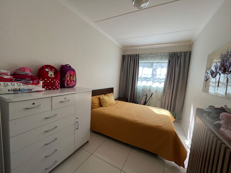 A functional bedroom featuring tiled flooring, neutral walls, and a window with curtain tracks, providing a clean and simple living space.