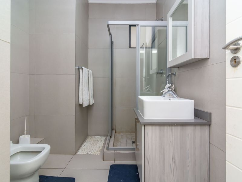 A modern bathroom featuring a glass shower enclosure, a vessel sink vanity with storage, and neutral wall tiling.