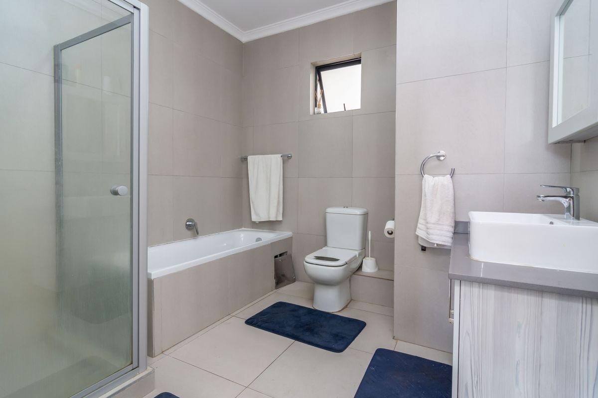 A modern bathroom featuring a glass-enclosed shower, a built-in bathtub, a vanity with a basin, and neutral wall-to-floor tiling.