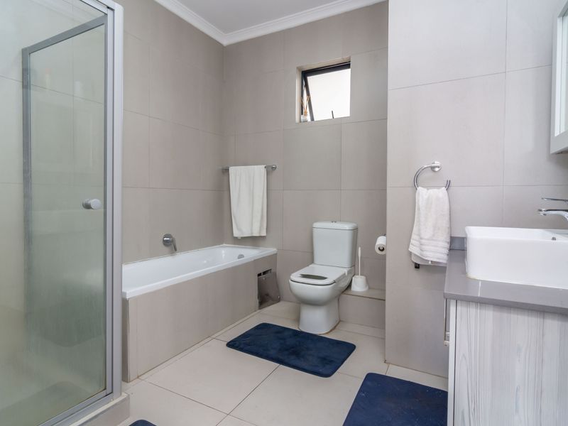A modern bathroom featuring a glass-enclosed shower, a built-in bathtub, a vanity with a basin, and neutral wall-to-floor tiling.