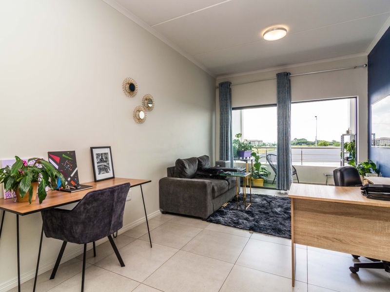 A bright living room featuring tiled flooring, an accent wall, and a large sliding glass door providing access to a balcony.