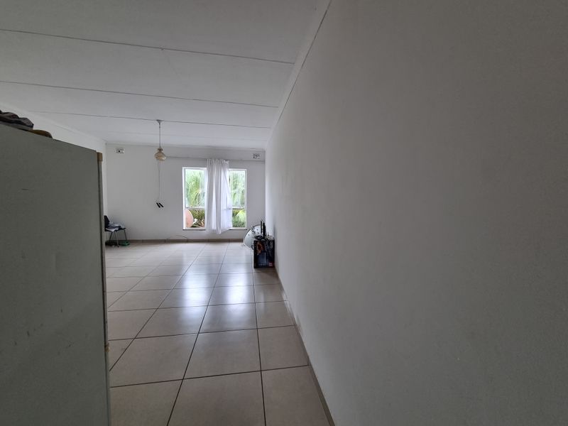 A spacious, empty living area featuring neutral tiled flooring and large windows, offering a blank canvas for interior design and renovation.