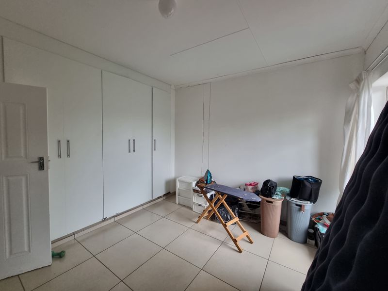 A bedroom featuring neutral tiled flooring and extensive white built-in cupboards providing ample storage space.