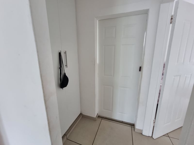 A functional hallway area featuring neutral tiled flooring and a built-in storage cupboard.