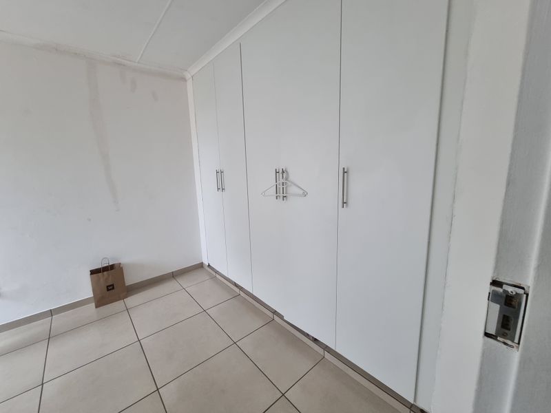 A vacant bedroom featuring built-in cupboards and tiled flooring, requiring minor cosmetic repairs to the walls and door hardware.