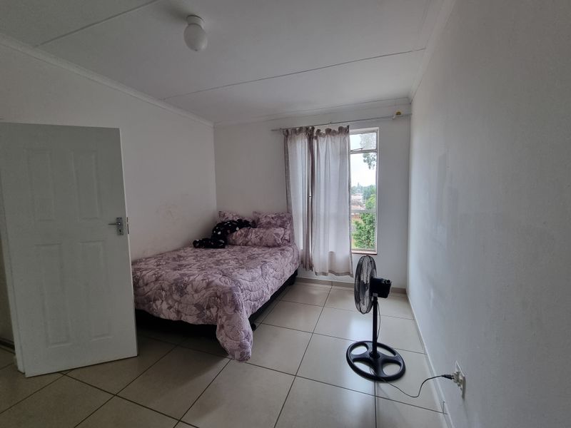 A simple bedroom featuring tiled flooring and a window with a curtain rail, requiring minor cosmetic updates to the wall finishes.