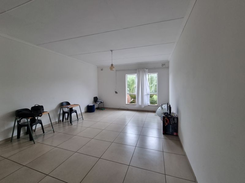 A spacious, neutrally finished living area featuring large format floor tiles and a simple pendant light, offering a blank canvas for interior design.