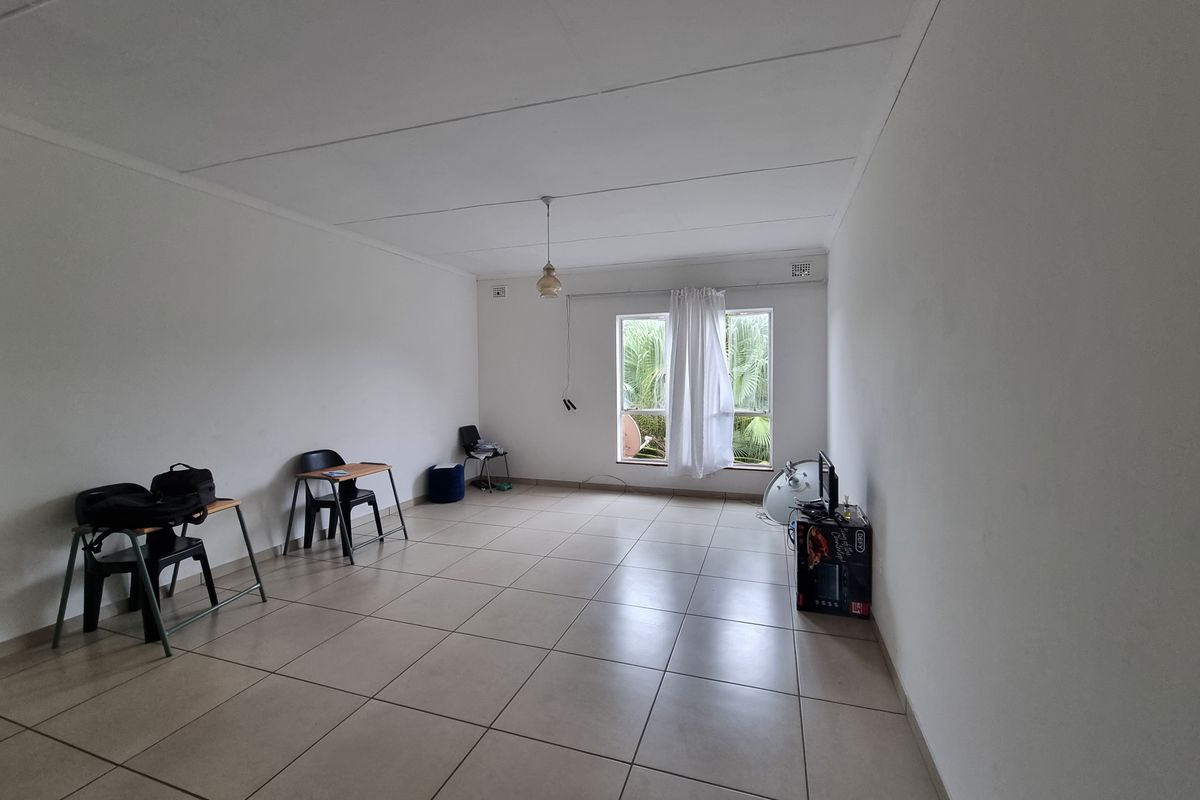 A spacious, neutrally finished living area featuring large format floor tiles and a simple pendant light, offering a blank canvas for interior design.