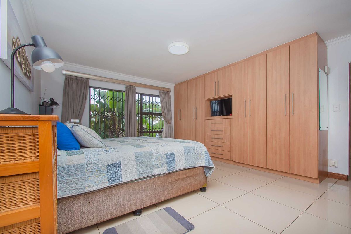 A well-maintained bedroom featuring extensive built-in wooden cabinetry, neutral tiled flooring, and security bars on the windows.