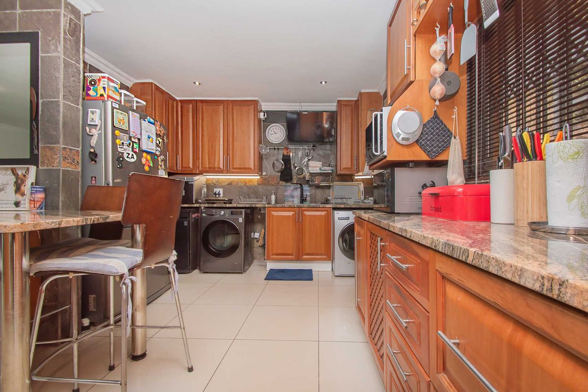 A functional kitchen featuring warm wooden cabinetry, granite countertops, stone wall accents, and integrated laundry appliances, offering a practical and well-utilized workspace.